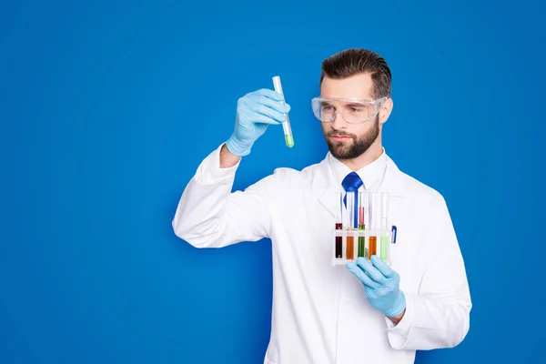 白ラボで無精髭を集中して科学者忙しいの肖像コート 手袋を分析 彼の腕は 灰色の背景に分離された複数の色液で試験管を見て — ストック写真