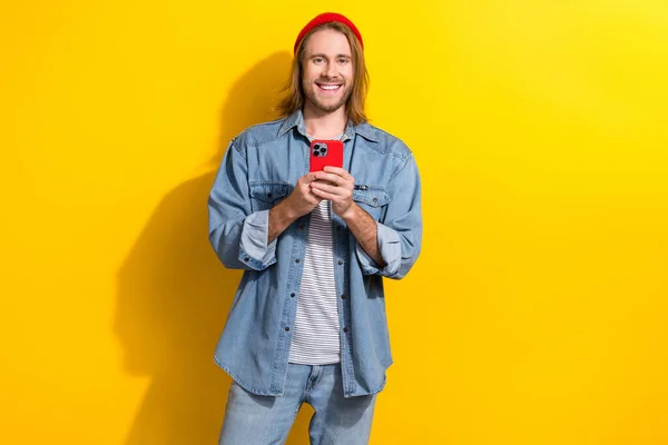 黄色の色の背景に隔離されたチャットスマートフォンを保持デニムジャケットを身に着けているボブの散髪とクールな陽気な肯定的な男の肖像 — ストック写真