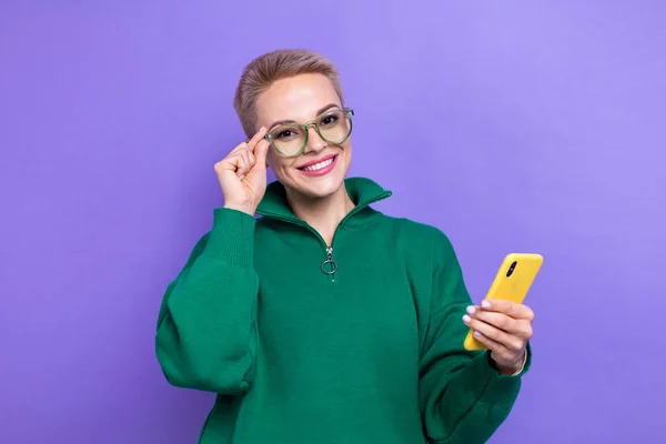 魅力的な正の女の子の写真短いブロンドのヘアスタイルのタッチ仕様眼鏡は 紫の色の背景に隔離された新しいアップルのIphoneのチェックフォロワーを保持 — ストック写真