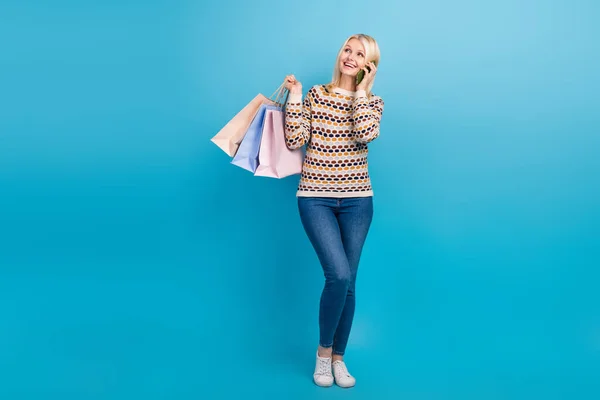 Full length portrait of charming nice person hold shop bags speak communicate telephone isolated on blue color background.