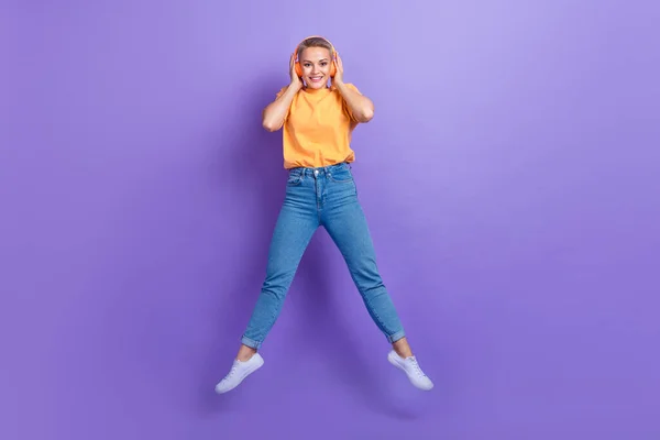 美しいです長さの写真可愛いです女の子服ジーンズホワイトスニーカージャンプ手タッチヘッドフォン孤立した上紫色の背景 — ストック写真