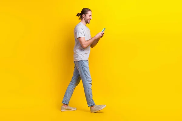 ハンサムな陽気な男のフルサイズの写真グレーのTシャツデニムパンツは空のスペースを見に行きますスマートフォンで隔離された黄色の色の背景 — ストック写真