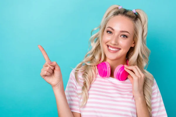 Photo of cute cheerful girl toothy smile touch headphones hang neck direct finger empty space isolated on teal color background.