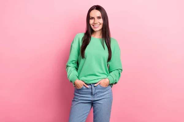 真っ直ぐな髪型をした楽観的な豪華な女性の写真緑のスウェットシャツはピンクの色の背景に隔離されたポケットに腕を保持 — ストック写真