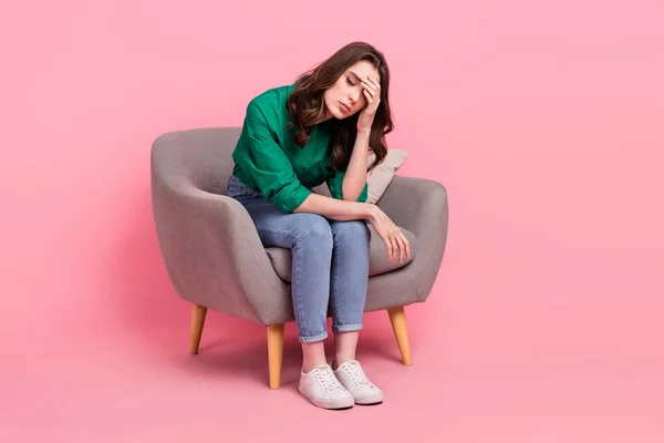 stock image Full size photo of upset gorgeous exhausted girl dressed jeans green shirt sit on armchair hand on forehead isolated on pink background.