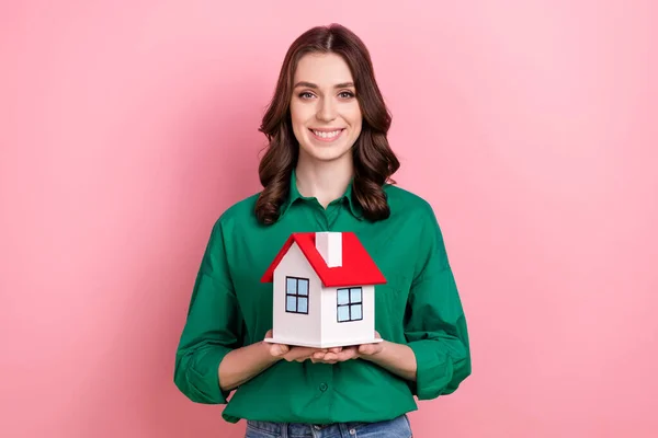 甜美迷人的女士身穿绿色衬衫 手持红色屋顶小木屋 粉色背景的照片 — 图库照片