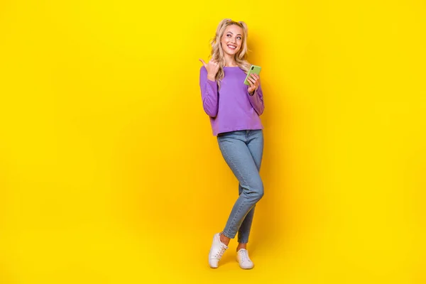 魅力的な若い女性のポイントのフルボディ写真は 空のスペースを見て5Gデバイスは黄色の色の背景に隔離された流行の紫の服を着用 — ストック写真