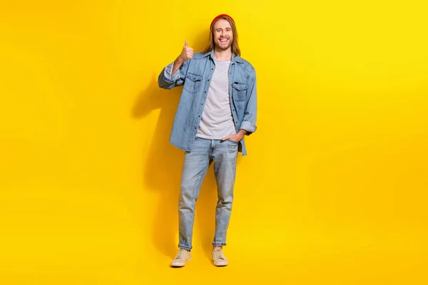 明るい楽観的な男のフルサイズの写真はデニムジャケットジーンズのズボンの靴を着用親指を示す上黄色の背景に孤立 — ストック写真