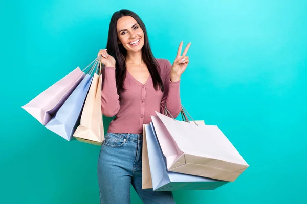 年轻购物狂女士的肖像照片显示V字你好符号拿着购物袋享受用青色背景独立购买的包裹 — 图库照片