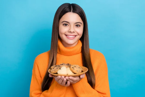 長い髪型と楽観的な陽気な女の子の写真は 青い色の背景に隔離されたクッキーとニットTurtleeck保持プレートを身に着けています — ストック写真