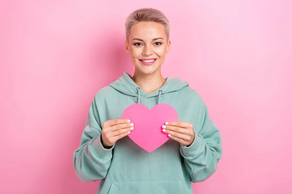 写真のかわいい陽気なブロンド短い髪の女の子ホールド紙の愛のシンボルポストカードバレンタインギフトからボーイフレンド隔離されたピンク色の背景 — ストック写真
