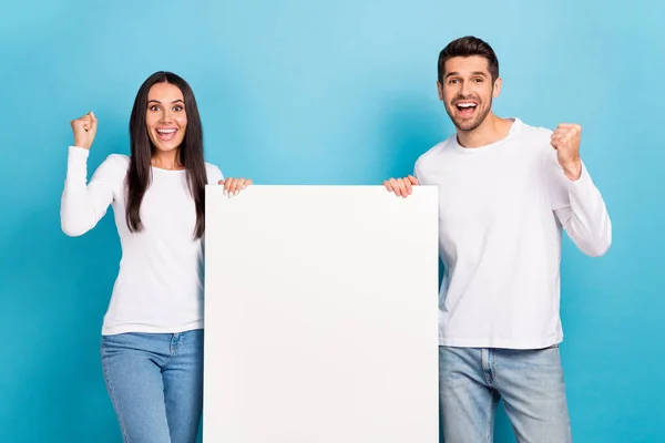 Photo of two delighted overjoyed people raise fists empty space blank isolated on blue color background.