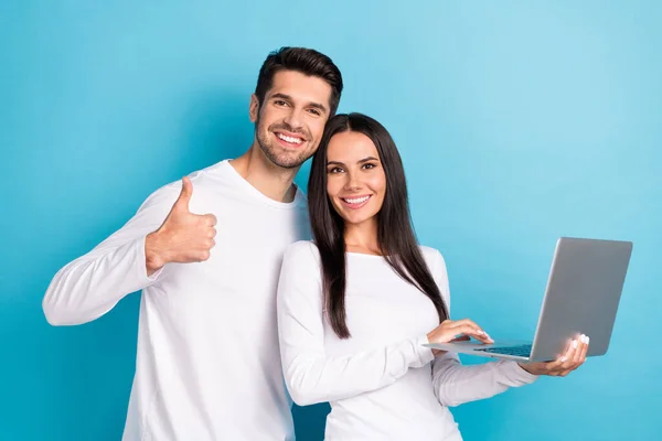 Photo of two cheerful pleasant cute couple people wear white shirts guy show like girl hold laptop isolated on blue color background.