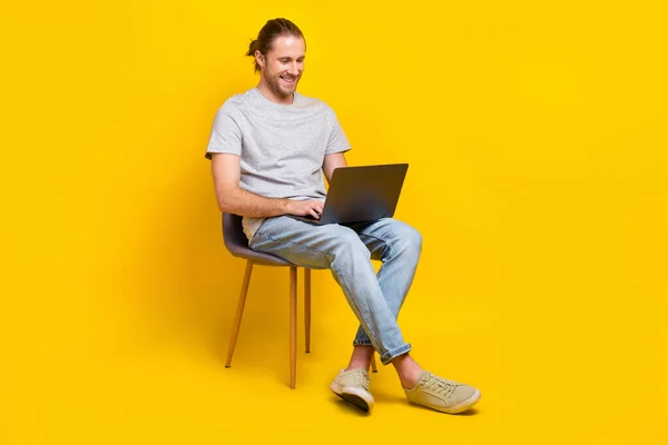 フルサイズ写真のハンサムな賢い男グレーTシャツパンツに座って上の椅子書き込みコード距離作業孤立した黄色の色背景 — ストック写真