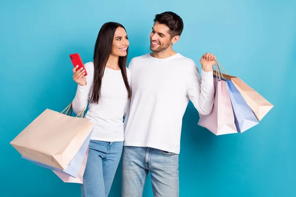 照片上 两个快乐的人拥抱在一起 面面相觑 拿着用蓝色背景隔开的购物袋 — 图库照片