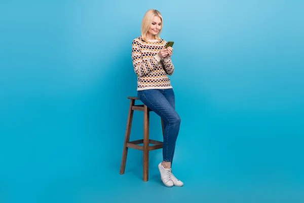 フルサイズポートレートの素敵な正の女性座って椅子使用電話タイピングポスト隔離された上の青の色の背景 — ストック写真