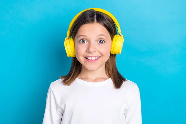 Photo of good mood schoolgirl with straight hairdo dressed white shirt headphones listen playlist isolated on blue color background.