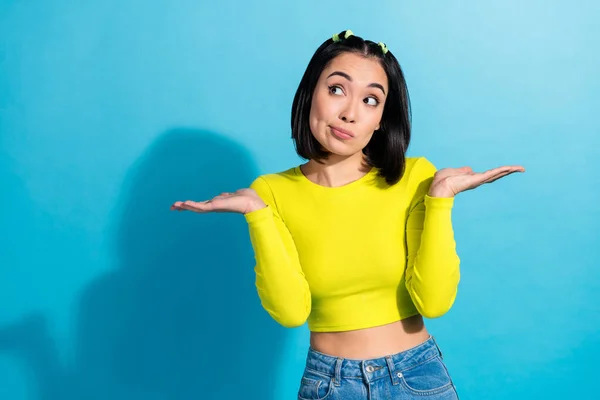 Photo of young slim belly korean girl shrug shoulders dont know answer your question how lose weight wear yellow shirt isolated on blue background.