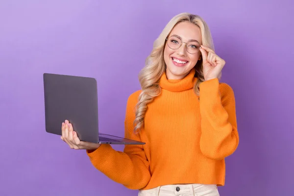 照片上可爱可爱的女孩 留着时髦的发型 穿着橙色毛衣 触摸眼镜 手持笔记本电脑 背景是紫色的 — 图库照片