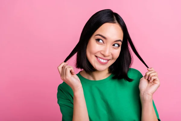 stock image Photo of good mood satisfied girl with bob hairdo wear green t-shirt look empty space touching curls isolated on pink color background.