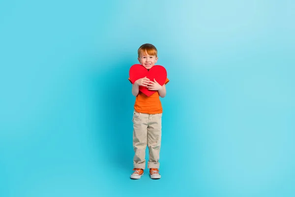 正の可愛い男の子の完全な長さの写真はオレンジスタイリッシュな服を保持赤い紙カードスタンド空のスペースに隔離されたシアン色の背景 — ストック写真