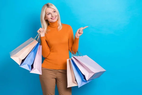 退休妇女穿着橙色毛衣袋购物狂的照片直指空空的地方新衣服品牌孤立在青色背景下 — 图库照片