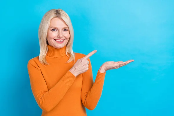 プロモーターの女性の写真ブロンドの髪はオレンジのタートルネックホールドパーム直接指格安食品広告の目新しさは 青の色の背景に隔離された — ストック写真