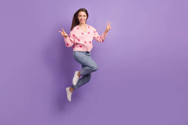 Full length photo of excited lady dressed strawberry cardigan showing v-sign jumping empty space isolated purple color background.