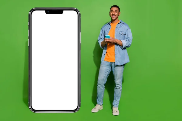 Full length photo of positive emotion man chatting with friends use big display phone isolated on green color background.