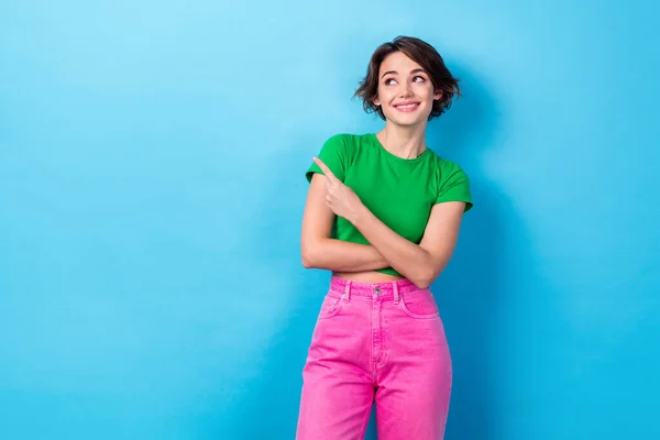 Photo of good mood dreamy lady dressed green top looking pointing finger empty space isolated blue color background.