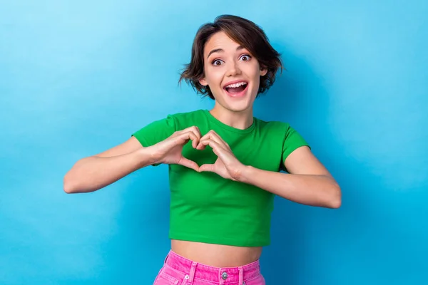 Photo of pretty excited lady dressed green top open mouth showing arms heart isolated blue color background.