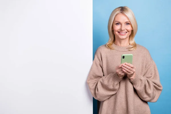 幸せな古いブロンドの髪の女性の写真ベージュのトレンディーなシャツホールド電話チェック新しいインターフェイスアプリのモックアップは 青の色の背景に隔離 — ストック写真