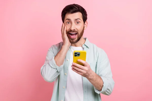 若い興奮男の写真タッチ頬のシャツを着用ホールドスマートフォン読書インターネットメディアニュースピンク色の背景に孤立 — ストック写真
