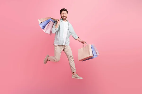 良い気分のフル長さの写真クールな男は 高上昇の買い物客をジャンプターコイズシャツを身に着けているピンク色の背景 — ストック写真