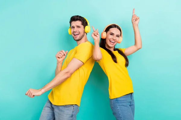 Photo of overjoyed crazy people dance listen enjoy music earphones fingers point up wear trendy yellow t-shirt isolated on cyan color background.
