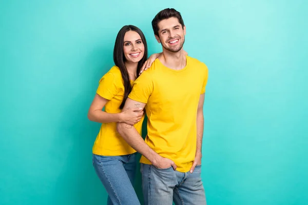 漂亮甜美的丈夫妻子穿着黄色T恤衫 拥抱着空旷的空间 孤零零的绿松石色背景 — 图库照片