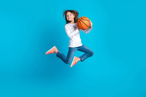 全长照片 一个快乐的女生穿着白衬衫牛仔裤运动鞋 带着蓝色背景的篮球飞舞 — 图库照片