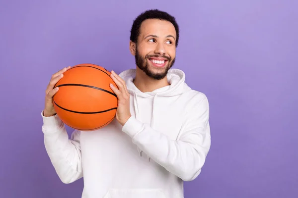 Portrait of positive minded man toothy smile hands hold basketball look empty space isolated on purple color background.
