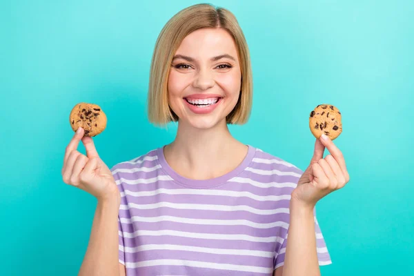 光沢のあるブロンドの髪の女の子の写真は トレンディーなTシャツの上昇手を身に着けている2おいしい甘いチョコレートクッキーは アクアマリン色の背景に隔離 — ストック写真