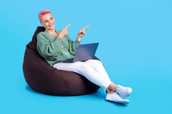 Full length photo of charming lady wear stylish outfit sit bean bag recommend modern device empty space isolated on blue color background.