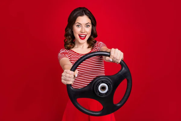滑稽兴奋的女司机拿着方向盘试车第一次穿条纹上衣孤立的红色背景的照片 — 图库照片