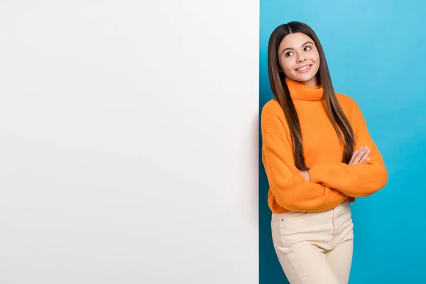 Photo of cute girl long hairstyle dressed knit turtleneck hold arms crossed look at board empty space isolated on blue color background.