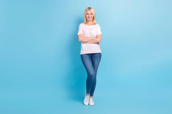 フルサイズの写真の良い気分シニア女性着用白いTシャツジーンズスニーカー立って腕が青の色の背景に孤立交差 — ストック写真