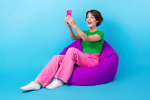 Stock image Full body photo of funny blogging girl hold smartphone recording video selfie sitting comfort pouf relax isolated on aquamarine color background.