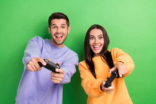 两个欣喜若狂的合作伙伴手牵着控制器在绿色背景下玩视频游戏的照片 — 图库照片