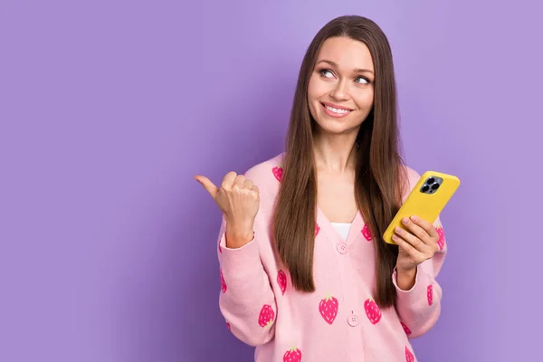 迷人的年轻女士棕色头发穿着羊毛衫的照片直指造型举行的Iphone新车型广告与紫色背景隔离 — 图库照片