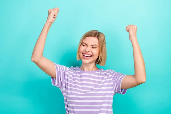 Portrait of optimistic woman with short haircut dressed stylish t-shirt raising fist up scream yeah isolated on teal color background.