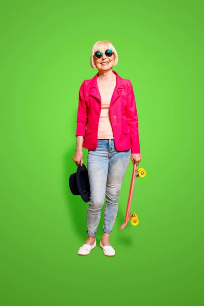 stock image Full-body full-legh vertical portrait of modern elderly woman with a board for skating isolated on brigth yellow background.