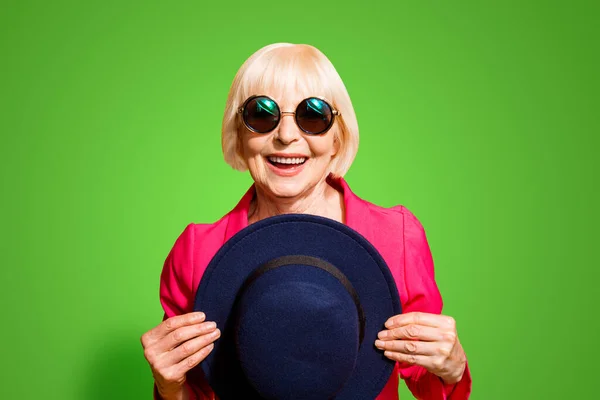 戴着夏日眼镜的老奶奶的画像在她的面前放着一顶黑色的帽子 在生动的黄色背景下 — 图库照片