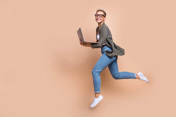 stock image Full length photo of busy excited woman wear khaki shirt jumping typing emails gadget emtpy space isolated beige color background.